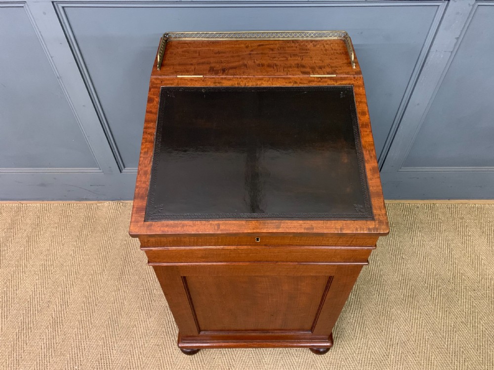 A George IV mahogany Davenport desk featuring a slanted brown leather writing surface, brass gallery rail, four side drawers with turned knobs, and bun feet. View V