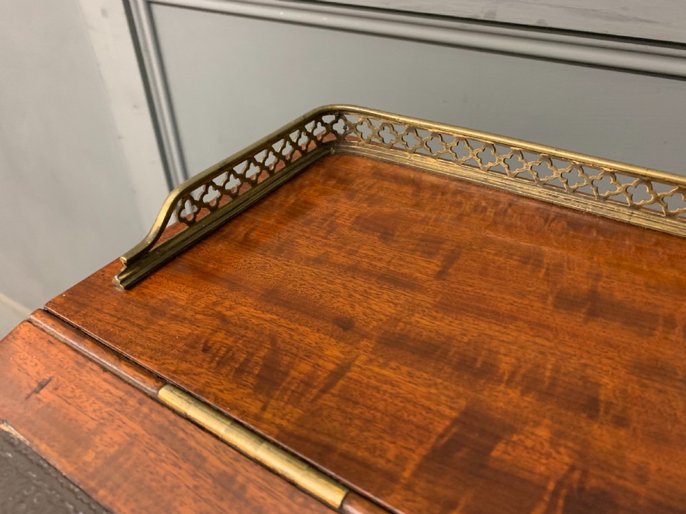 A George IV mahogany Davenport desk featuring a slanted brown leather writing surface, brass gallery rail, four side drawers with turned knobs, and bun feet. View VI