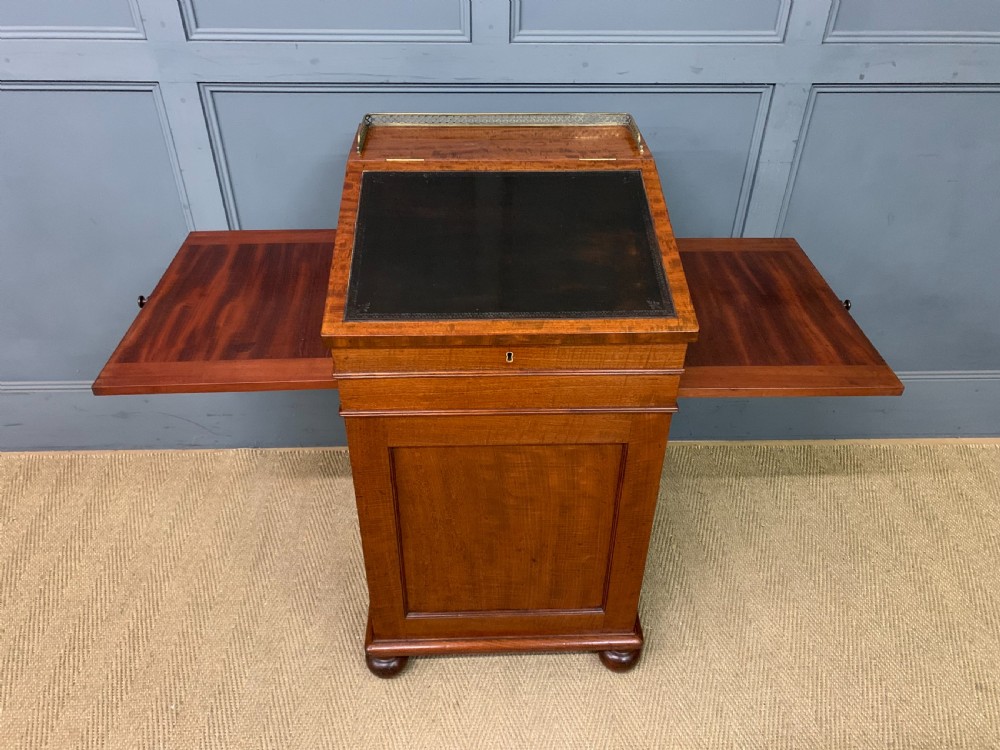 A George IV mahogany Davenport desk featuring a slanted brown leather writing surface, brass gallery rail, four side drawers with turned knobs, and bun feet. View XV