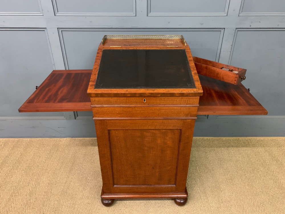 A George IV mahogany Davenport desk featuring a slanted brown leather writing surface, brass gallery rail, four side drawers with turned knobs, and bun feet. View XVI
