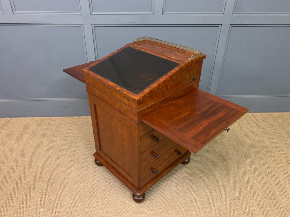 A George IV mahogany Davenport desk featuring a slanted brown leather writing surface, brass gallery rail, four side drawers with turned knobs, and bun feet. View XIX