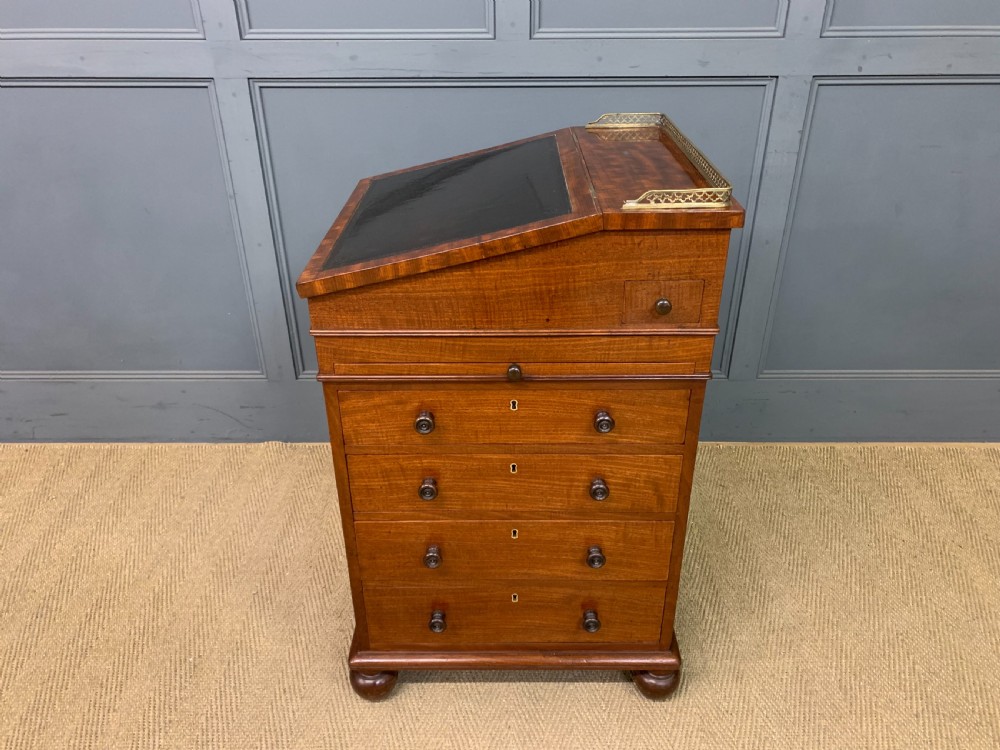 A George IV mahogany Davenport desk featuring a slanted brown leather writing surface, brass gallery rail, four side drawers with turned knobs, and bun feet. View XXVII