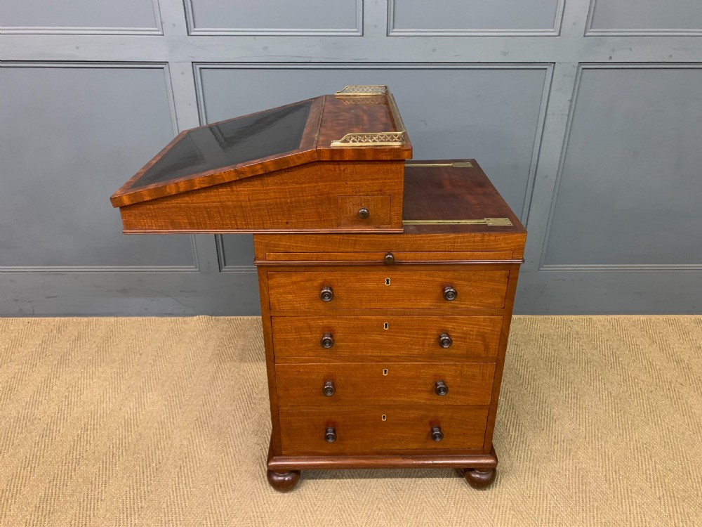 A George IV mahogany Davenport desk featuring a slanted brown leather writing surface, brass gallery rail, four side drawers with turned knobs, and bun feet. View XXVIII