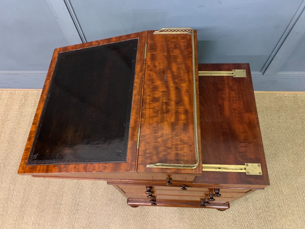 A George IV mahogany Davenport desk featuring a slanted brown leather writing surface, brass gallery rail, four side drawers with turned knobs, and bun feet. View XXIX