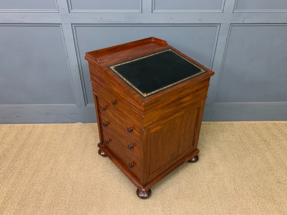 An early Victorian mahogany Davenport desk with a sloped leather writing surface and side drawers.