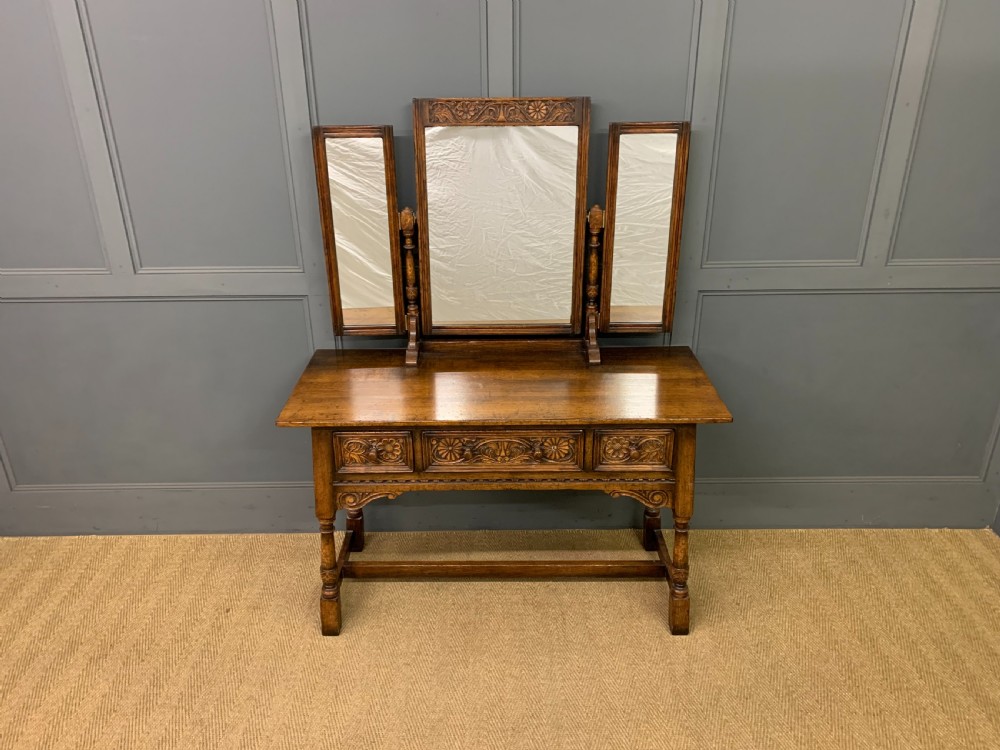 A carved oak dressing table featuring a central tri-fold mirror, three carved drawers, turned legs, and an accompanying stool upholstered in purple patterned fabric. View III