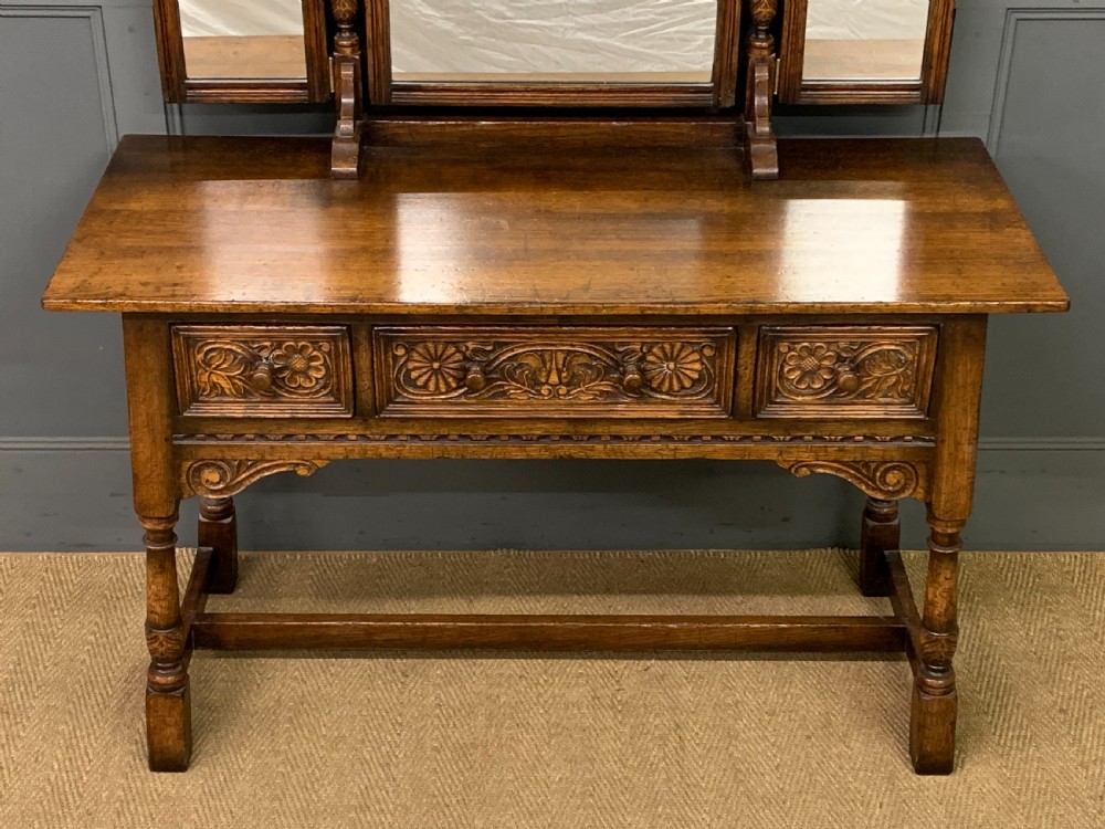 A carved oak dressing table featuring a central tri-fold mirror, three carved drawers, turned legs, and an accompanying stool upholstered in purple patterned fabric. View IV