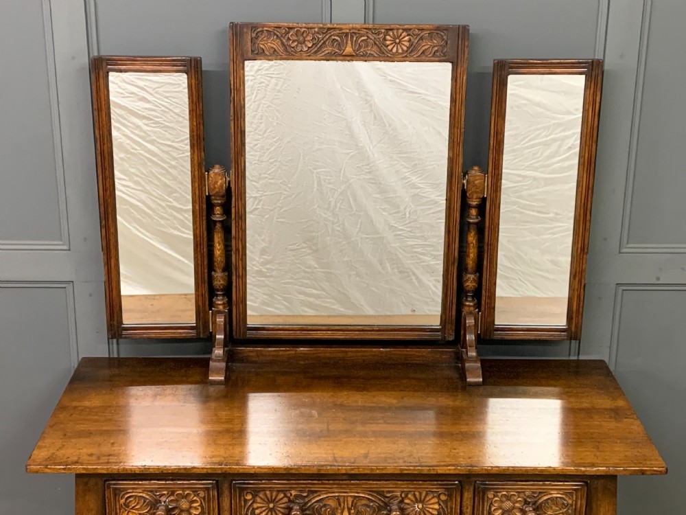 A carved oak dressing table featuring a central tri-fold mirror, three carved drawers, turned legs, and an accompanying stool upholstered in purple patterned fabric. View VI
