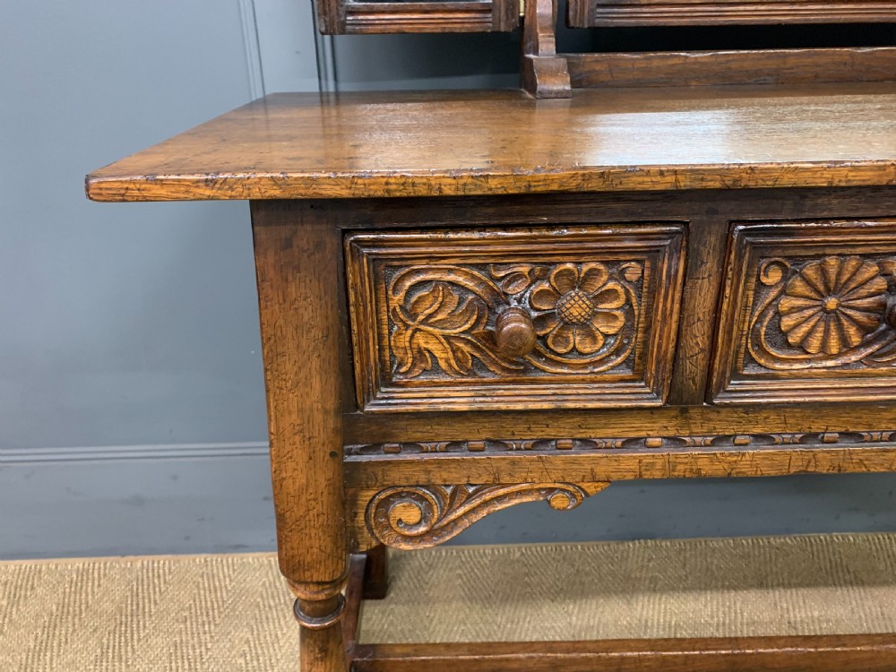 A carved oak dressing table featuring a central tri-fold mirror, three carved drawers, turned legs, and an accompanying stool upholstered in purple patterned fabric. View VII