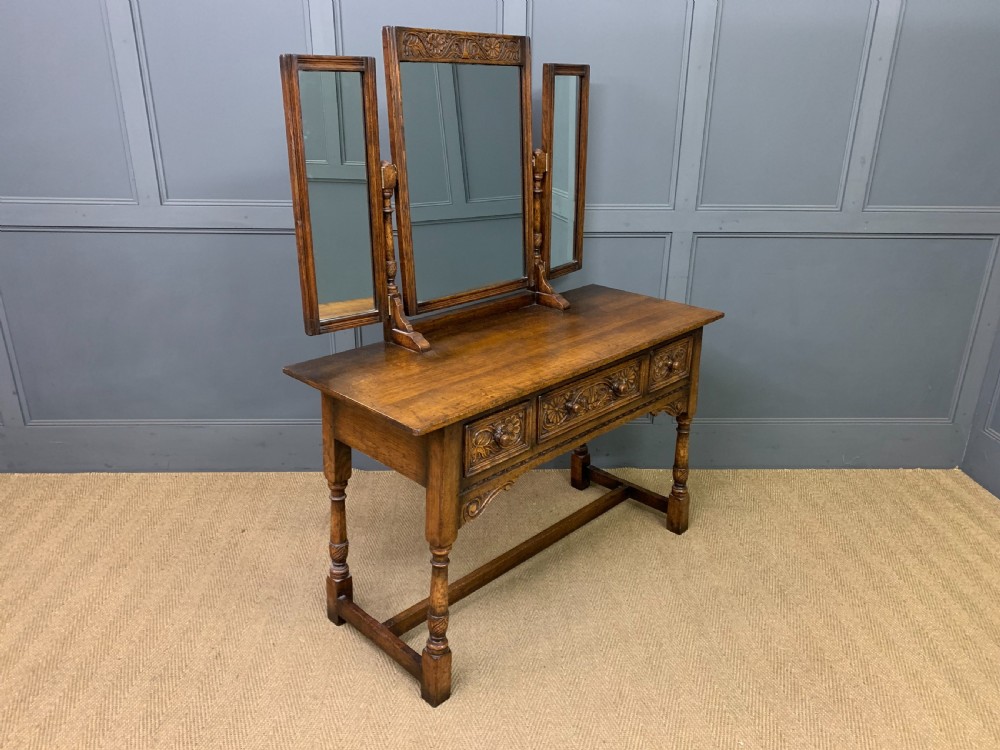 A carved oak dressing table featuring a central tri-fold mirror, three carved drawers, turned legs, and an accompanying stool upholstered in purple patterned fabric. View VIII