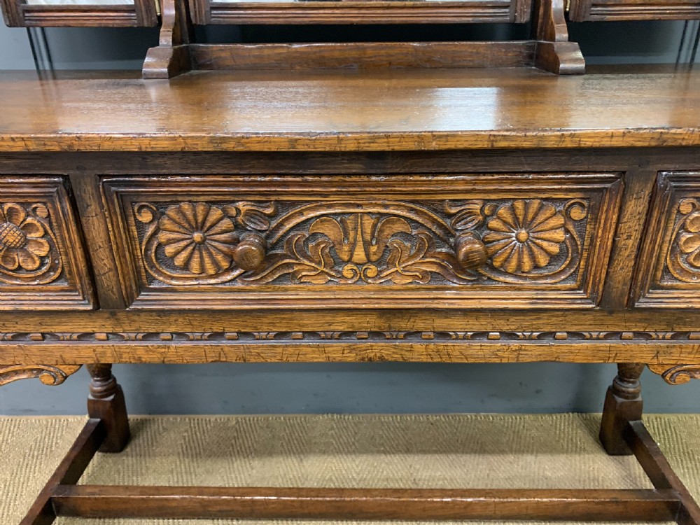 A carved oak dressing table featuring a central tri-fold mirror, three carved drawers, turned legs, and an accompanying stool upholstered in purple patterned fabric. View IX