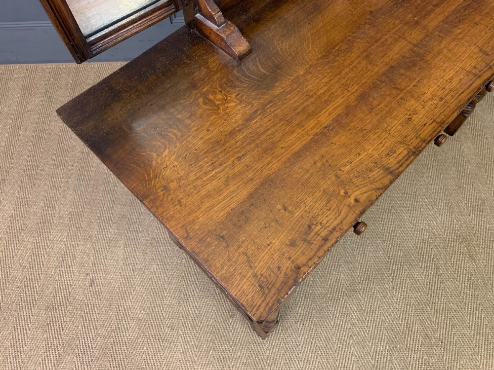 A carved oak dressing table featuring a central tri-fold mirror, three carved drawers, turned legs, and an accompanying stool upholstered in purple patterned fabric. View X