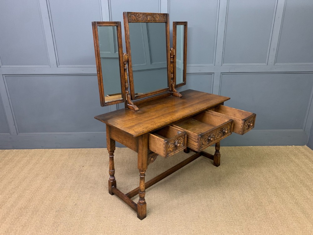A carved oak dressing table featuring a central tri-fold mirror, three carved drawers, turned legs, and an accompanying stool upholstered in purple patterned fabric. View XI