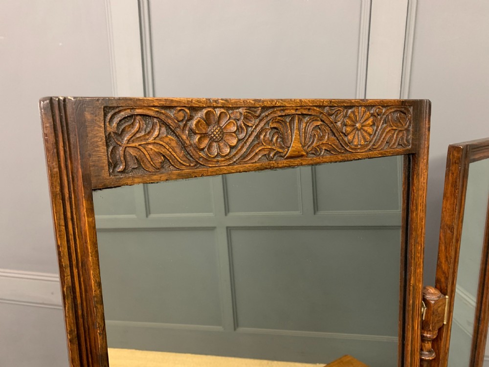 A carved oak dressing table featuring a central tri-fold mirror, three carved drawers, turned legs, and an accompanying stool upholstered in purple patterned fabric. View XII