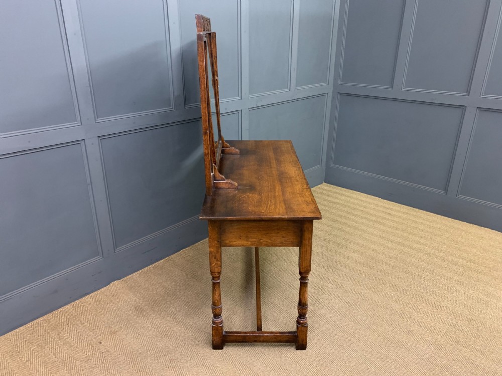 A carved oak dressing table featuring a central tri-fold mirror, three carved drawers, turned legs, and an accompanying stool upholstered in purple patterned fabric. View XIII