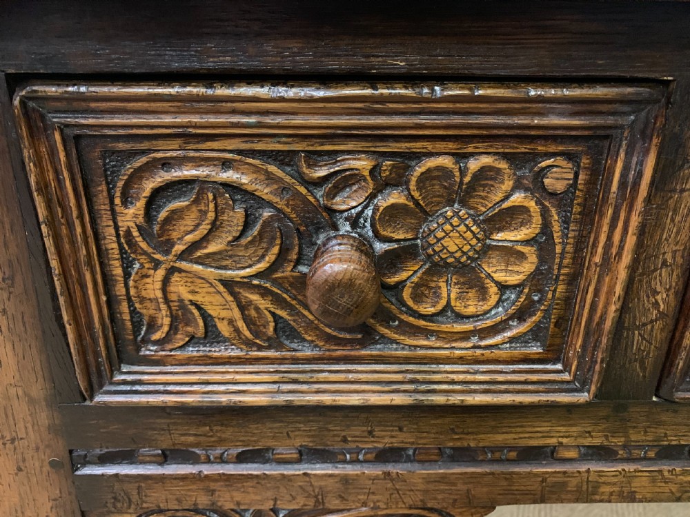 A carved oak dressing table featuring a central tri-fold mirror, three carved drawers, turned legs, and an accompanying stool upholstered in purple patterned fabric. View XVI
