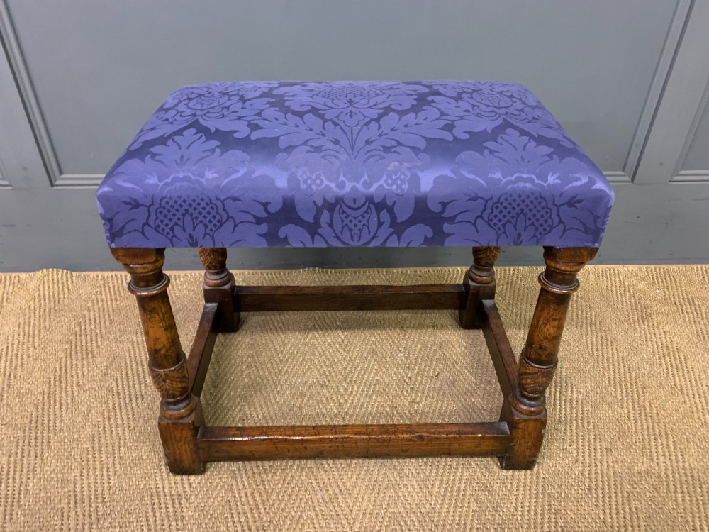 A carved oak dressing table featuring a central tri-fold mirror, three carved drawers, turned legs, and an accompanying stool upholstered in purple patterned fabric. View XVII