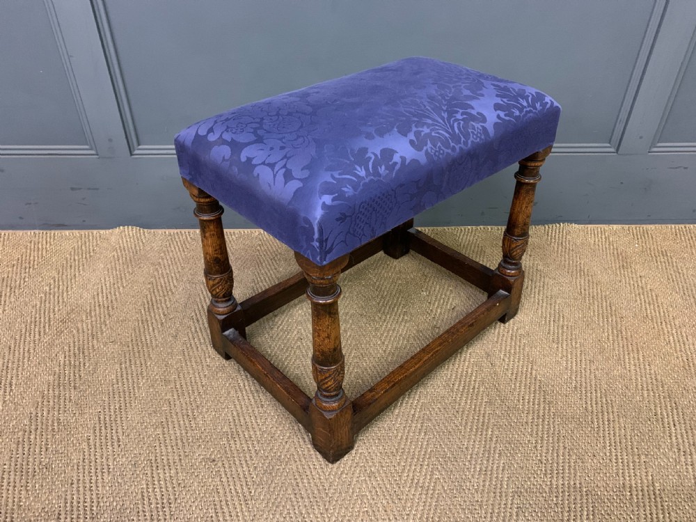 A carved oak dressing table featuring a central tri-fold mirror, three carved drawers, turned legs, and an accompanying stool upholstered in purple patterned fabric. View XVIII