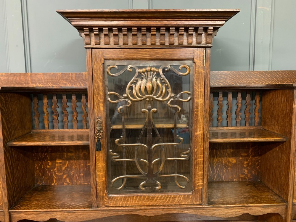 An Arts and Crafts oak sideboard featuring detailed inlaid floral marquetry panels, a central leaded glass upper cabinet, and decorative copper hardware. View VI