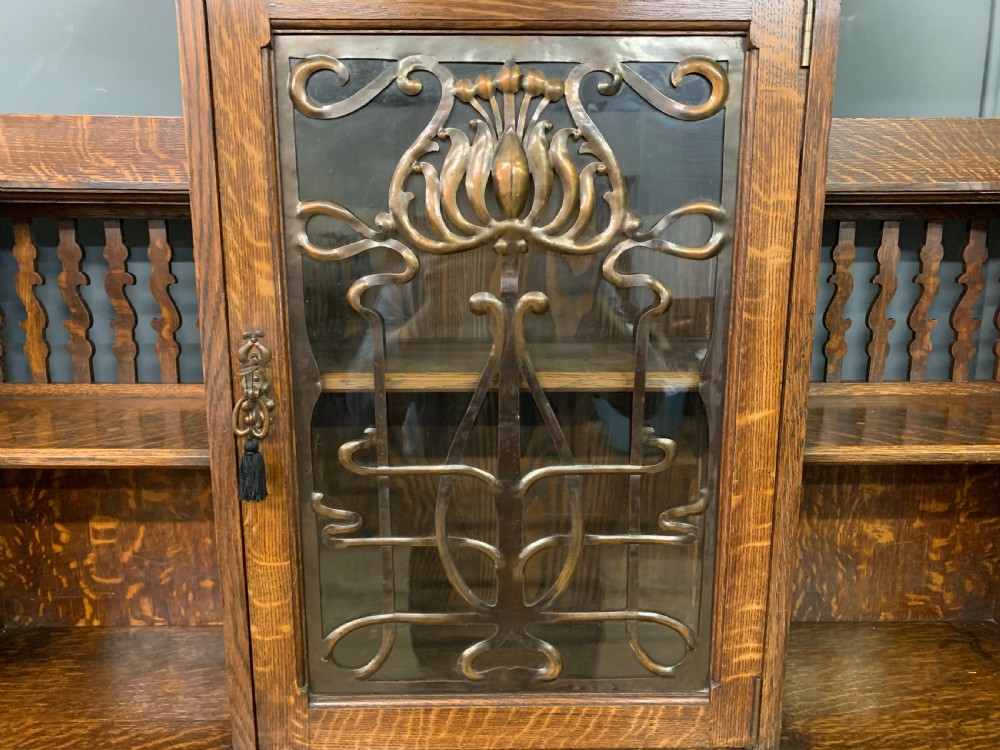 An Arts and Crafts oak sideboard featuring detailed inlaid floral marquetry panels, a central leaded glass upper cabinet, and decorative copper hardware. View VII