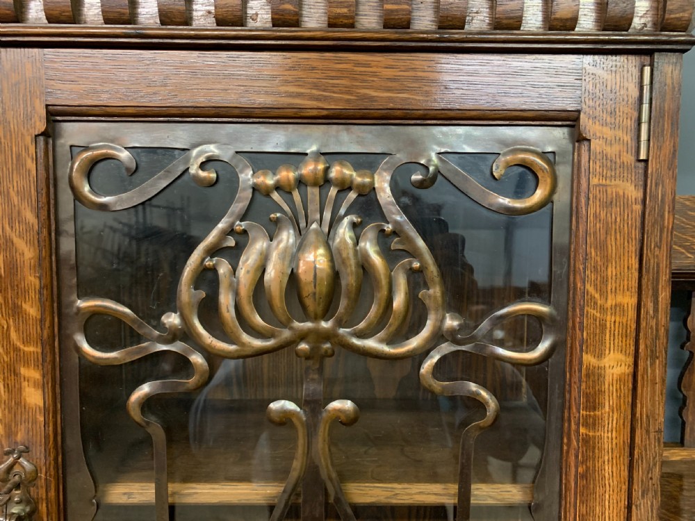 An Arts and Crafts oak sideboard featuring detailed inlaid floral marquetry panels, a central leaded glass upper cabinet, and decorative copper hardware. View VIII