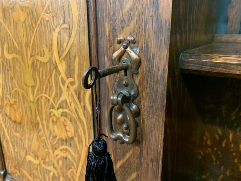 An Arts and Crafts oak sideboard featuring detailed inlaid floral marquetry panels, a central leaded glass upper cabinet, and decorative copper hardware. View IX