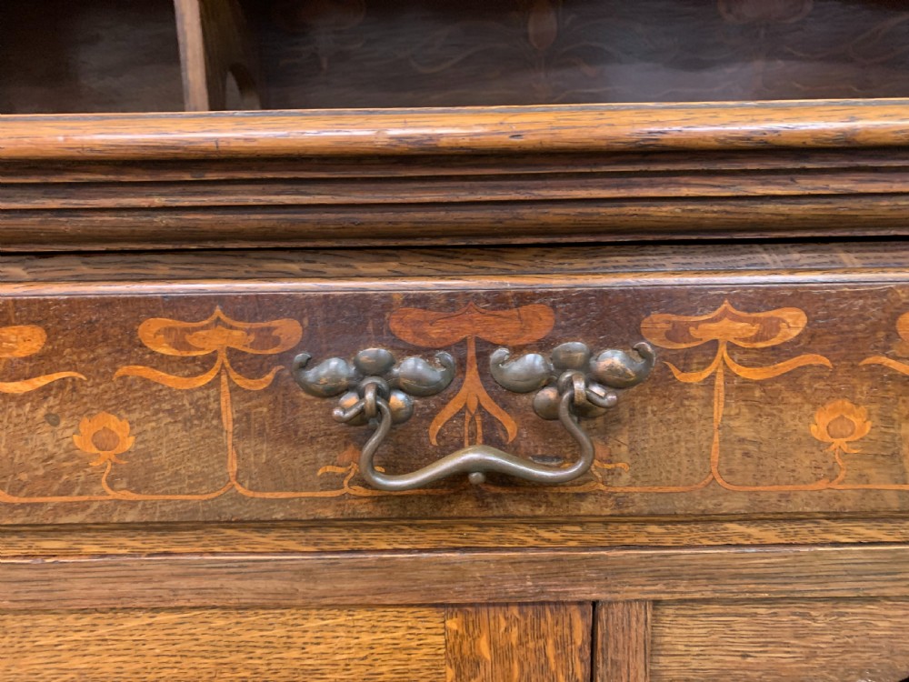 An Arts and Crafts oak sideboard featuring detailed inlaid floral marquetry panels, a central leaded glass upper cabinet, and decorative copper hardware. View XI