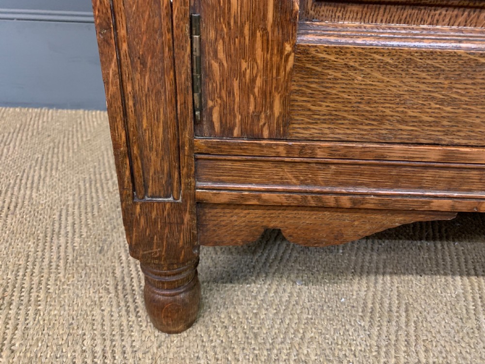 An Arts and Crafts oak sideboard featuring detailed inlaid floral marquetry panels, a central leaded glass upper cabinet, and decorative copper hardware. View XIII