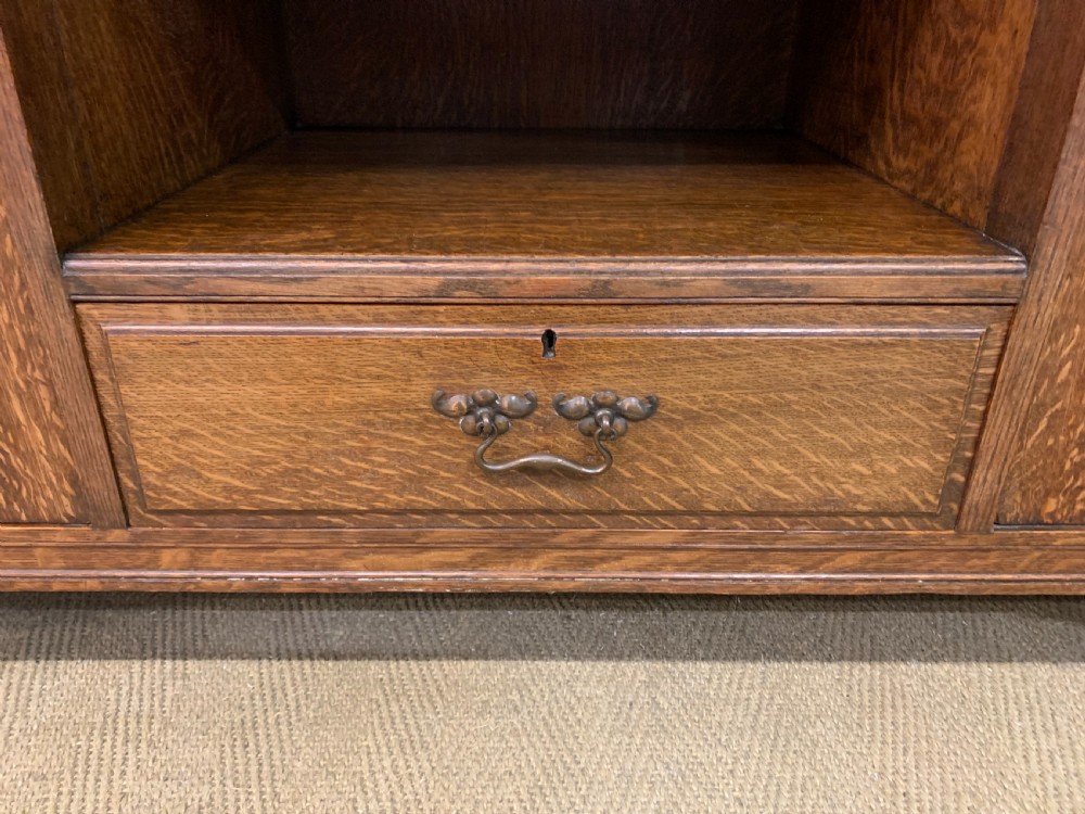 An Arts and Crafts oak sideboard featuring detailed inlaid floral marquetry panels, a central leaded glass upper cabinet, and decorative copper hardware. View XV