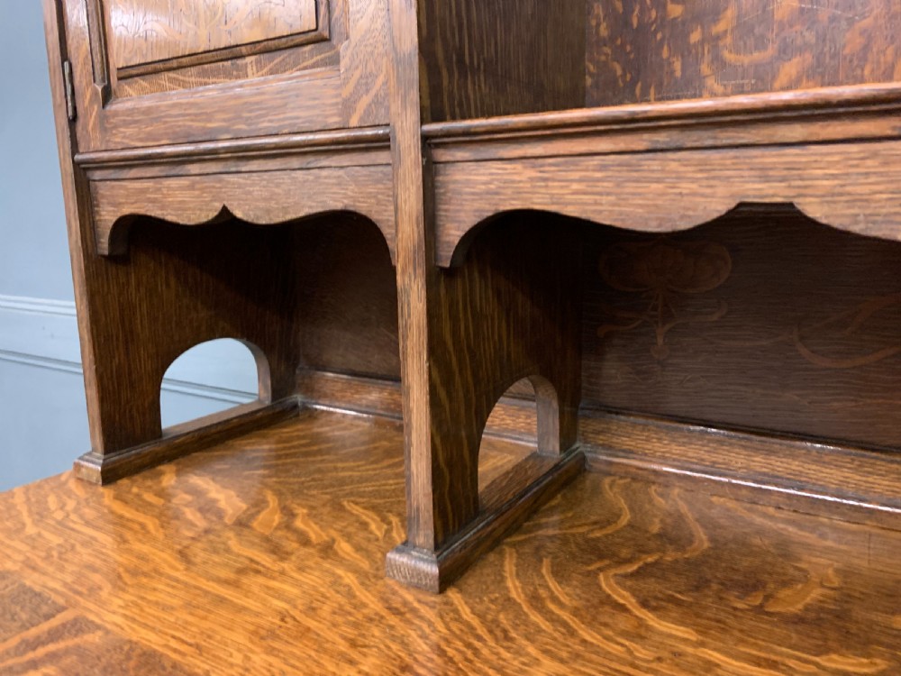 An Arts and Crafts oak sideboard featuring detailed inlaid floral marquetry panels, a central leaded glass upper cabinet, and decorative copper hardware. View XXI