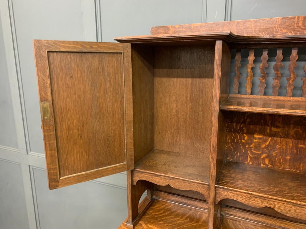 An Arts and Crafts oak sideboard featuring detailed inlaid floral marquetry panels, a central leaded glass upper cabinet, and decorative copper hardware. View XXIV