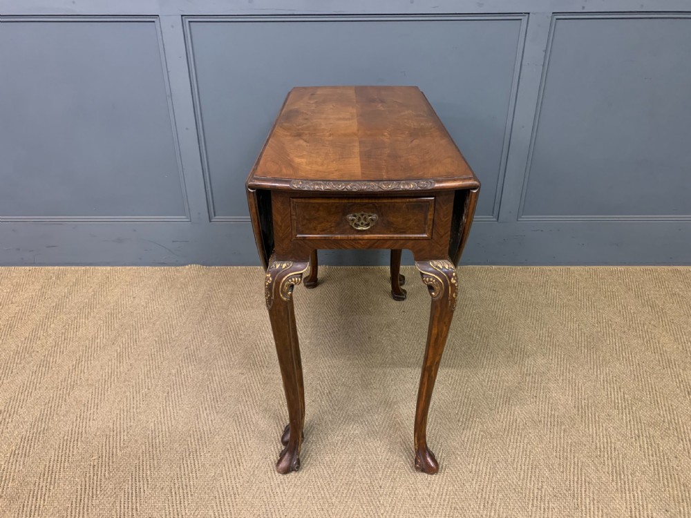 A burr walnut drop flap table featuring carved cabriole legs with leaf decoration, a single drawer with brass pull, and two rounded drop leaves. View II