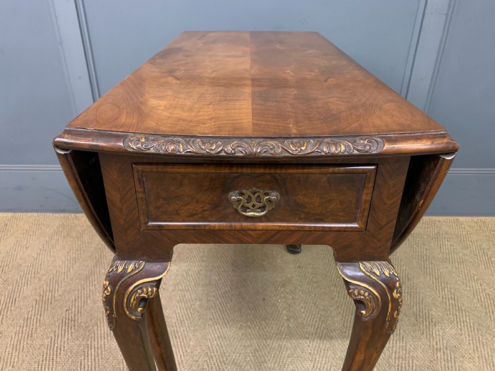 A burr walnut drop flap table featuring carved cabriole legs with leaf decoration, a single drawer with brass pull, and two rounded drop leaves. View III