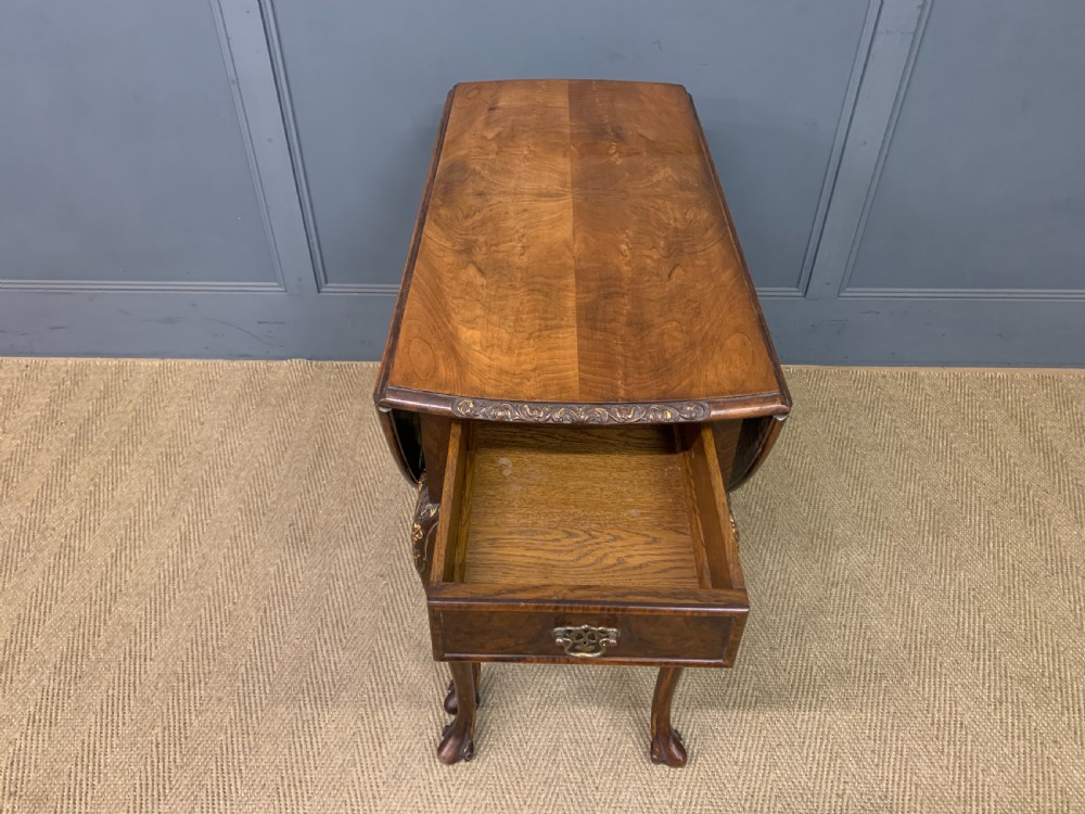 A burr walnut drop flap table featuring carved cabriole legs with leaf decoration, a single drawer with brass pull, and two rounded drop leaves. View IV