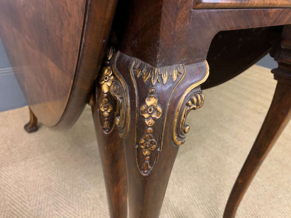A burr walnut drop flap table featuring carved cabriole legs with leaf decoration, a single drawer with brass pull, and two rounded drop leaves. View V