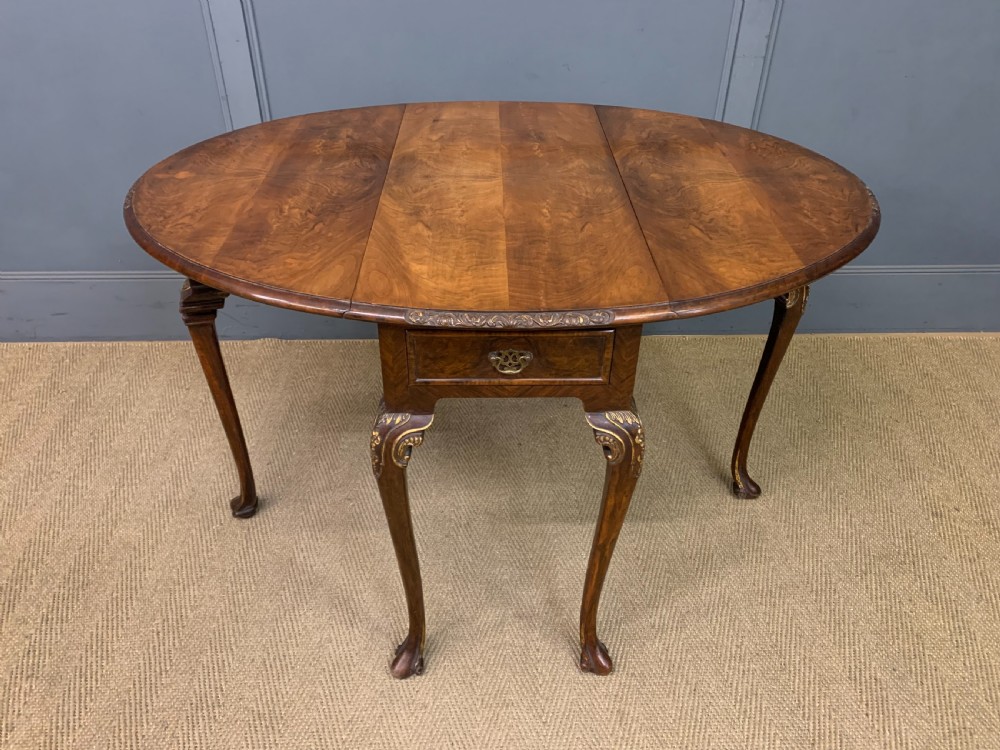 A burr walnut drop flap table featuring carved cabriole legs with leaf decoration, a single drawer with brass pull, and two rounded drop leaves. View VII