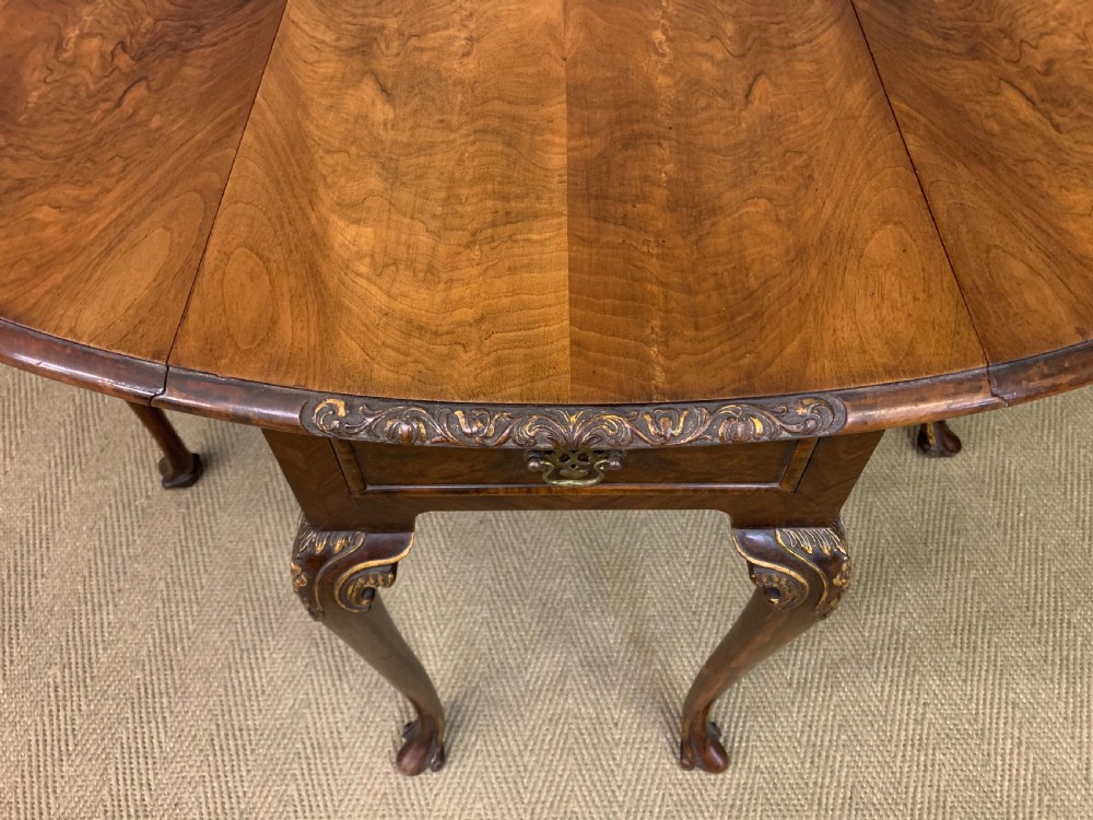 A burr walnut drop flap table featuring carved cabriole legs with leaf decoration, a single drawer with brass pull, and two rounded drop leaves. View VIII