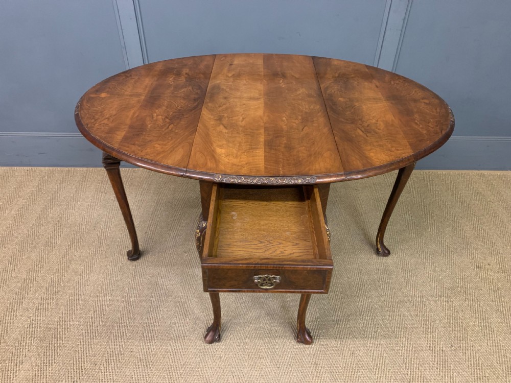 A burr walnut drop flap table featuring carved cabriole legs with leaf decoration, a single drawer with brass pull, and two rounded drop leaves. View XI