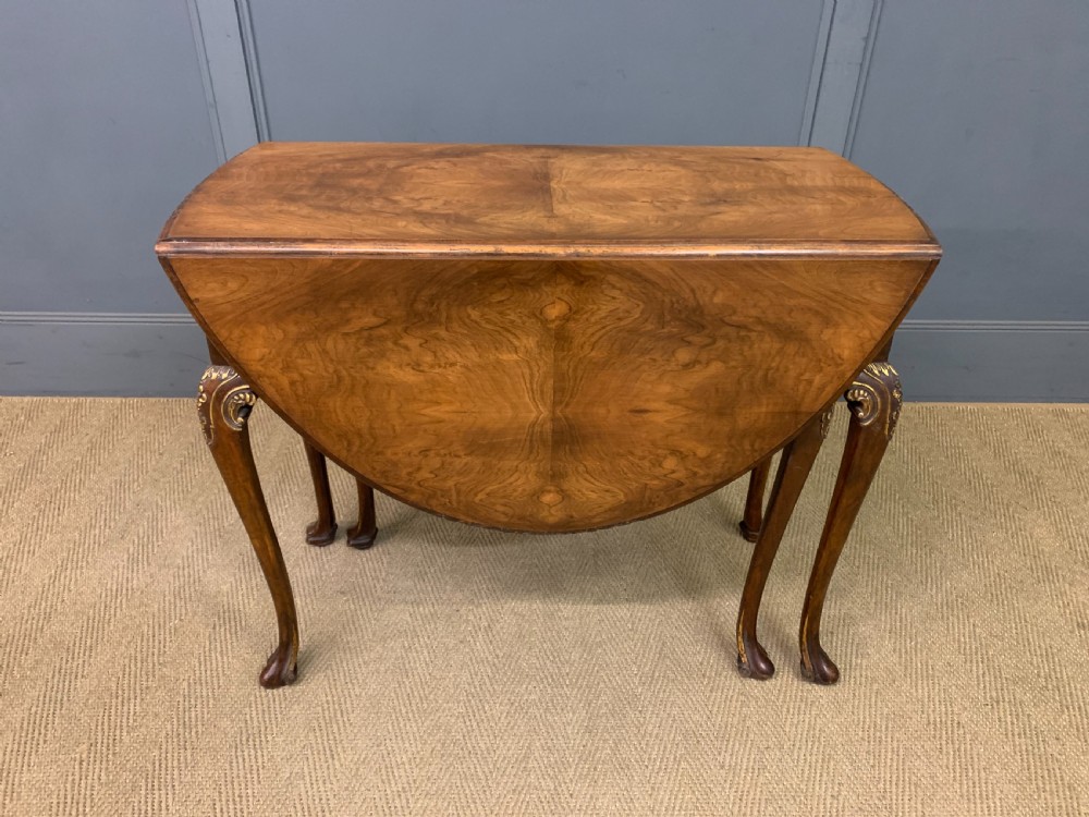A burr walnut drop flap table featuring carved cabriole legs with leaf decoration, a single drawer with brass pull, and two rounded drop leaves. View XIV