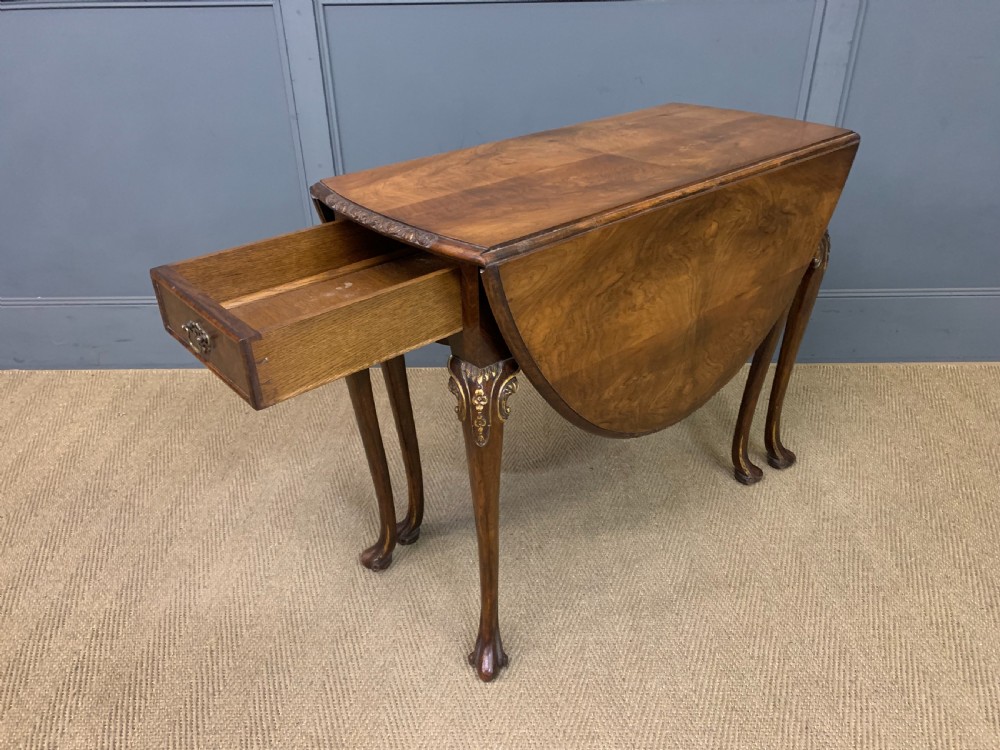 A burr walnut drop flap table featuring carved cabriole legs with leaf decoration, a single drawer with brass pull, and two rounded drop leaves. View XV