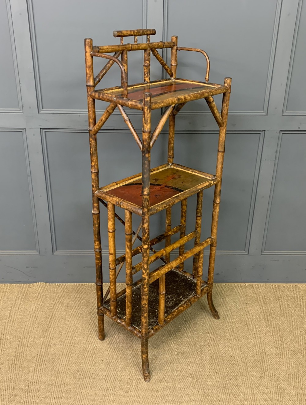 A late Victorian three-tiered bamboo whatnot stand featuring lacquer wood panel surfaces and vertical lower divisions.