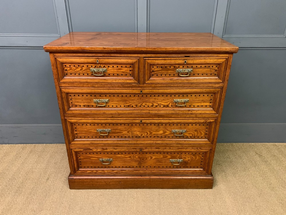 A late Victorian pitch pine chest of drawers featuring ebonised geometric dot inlay details and brass drop handles.