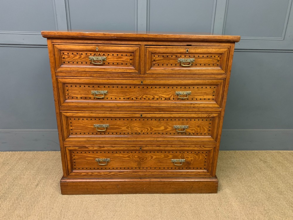 A late Victorian pitch pine chest of drawers featuring ebonised geometric dot inlay details and brass drop handles. View II
