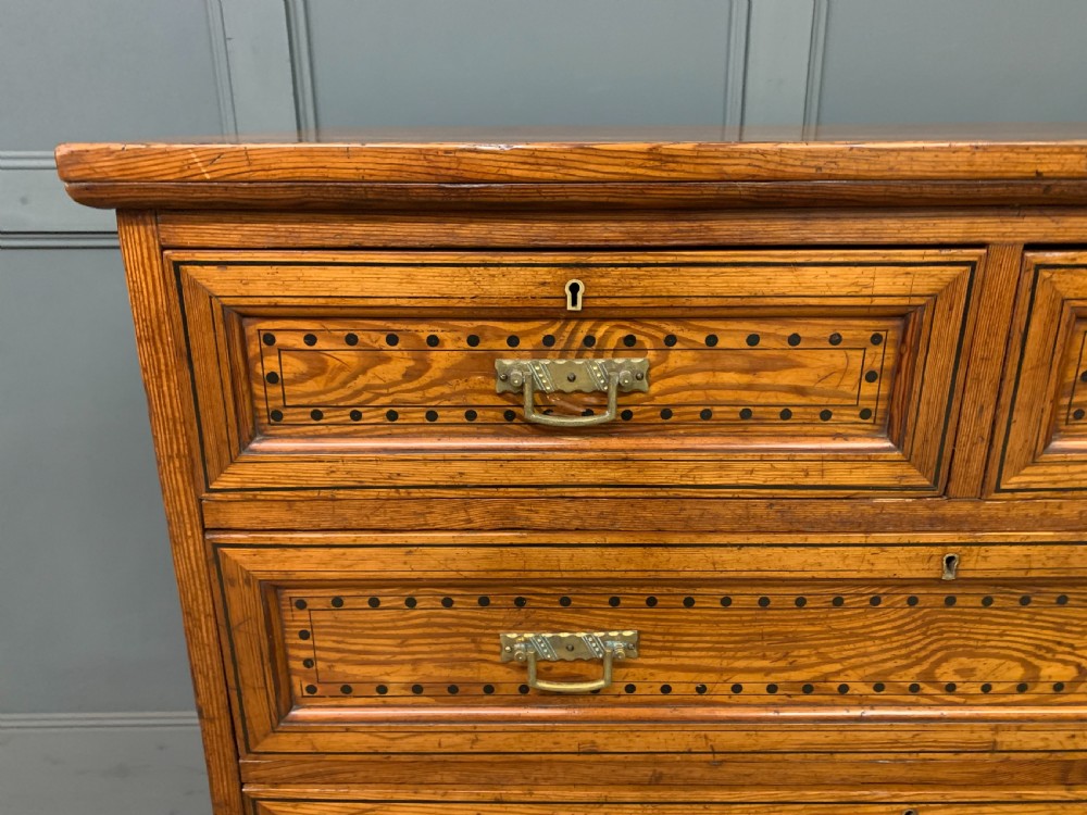 A late Victorian pitch pine chest of drawers featuring ebonised geometric dot inlay details and brass drop handles. View IV
