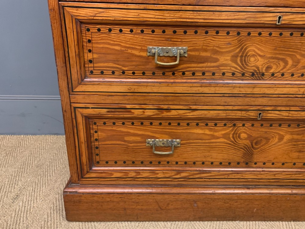 A late Victorian pitch pine chest of drawers featuring ebonised geometric dot inlay details and brass drop handles. View V