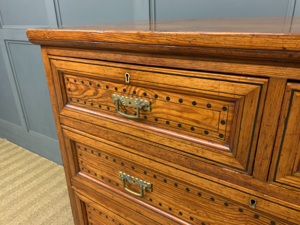 A late Victorian pitch pine chest of drawers featuring ebonised geometric dot inlay details and brass drop handles. View VI