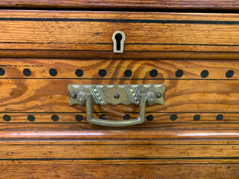 A late Victorian pitch pine chest of drawers featuring ebonised geometric dot inlay details and brass drop handles. View VII