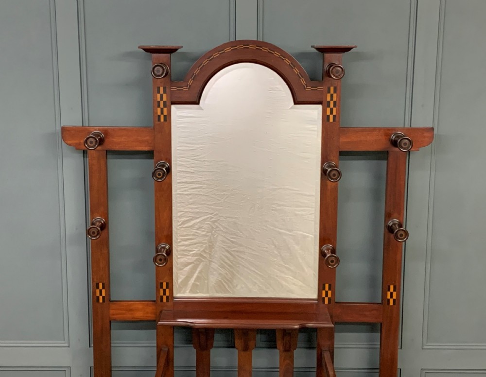 An Arts and Crafts inlaid mahogany hall stand featuring an arched central mirror, coat pegs, marble surface, and integrated umbrella racks. View II