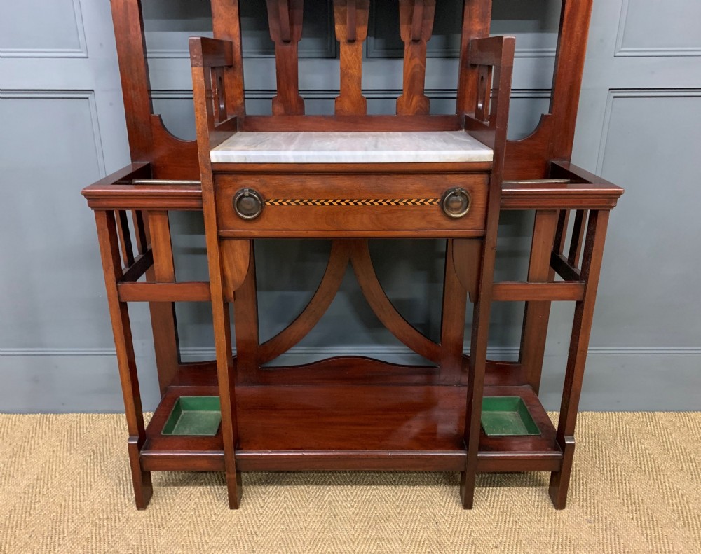 An Arts and Crafts inlaid mahogany hall stand featuring an arched central mirror, coat pegs, marble surface, and integrated umbrella racks. View IV