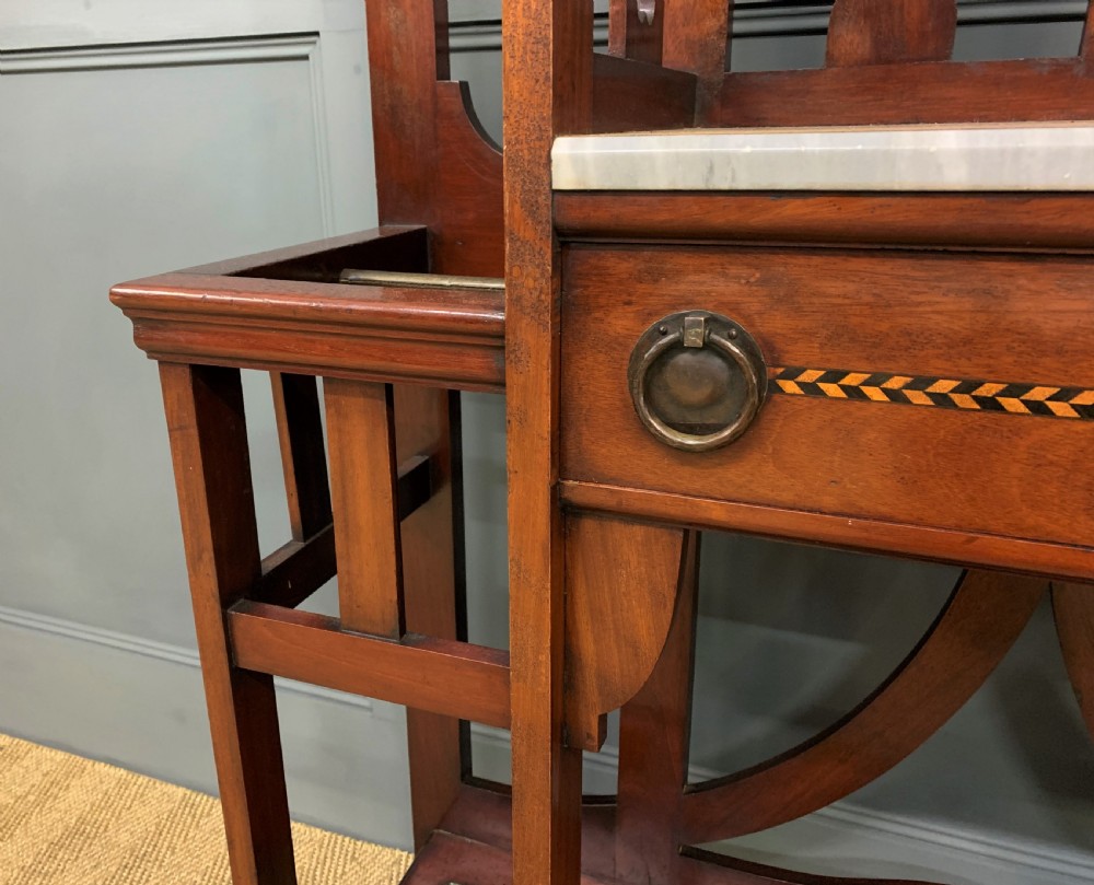 An Arts and Crafts inlaid mahogany hall stand featuring an arched central mirror, coat pegs, marble surface, and integrated umbrella racks. View V